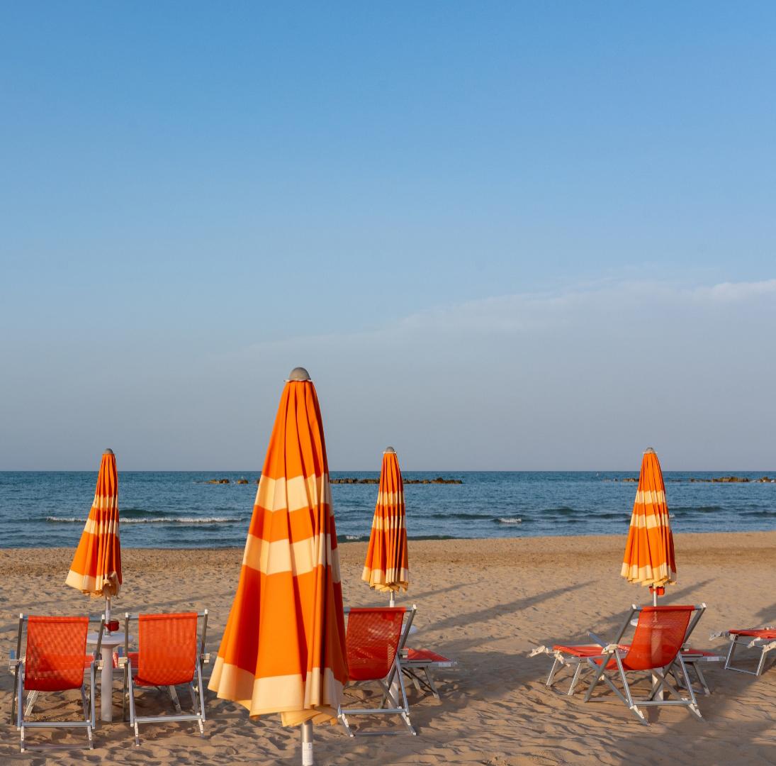 Spiaggia serena con ombrelloni arancioni chiusi, mare calmo e cielo limpido.
