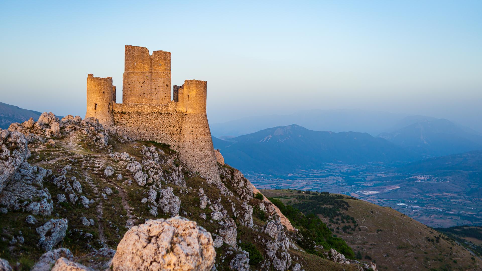 Antico castello su montagna, al tramonto, con vista mozzafiato sulla valle sottostante.