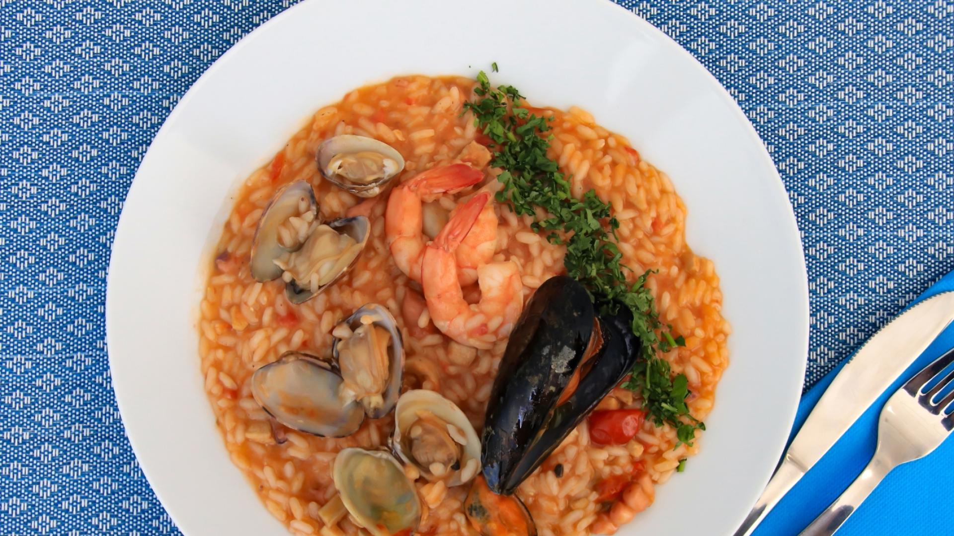 Risotto ai frutti di mare, colorato e invitante, su tovaglia blu, con posate lucenti.