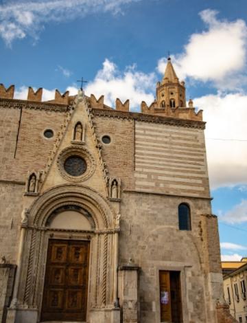 Facciata gotica di una chiesa con cielo azzurro e nuvole bianche, atmosfera serena.