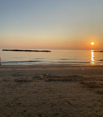 Tramonto sereno sul mare calmo, riflessi dorati e spiaggia tranquilla evocano pace e bellezza.