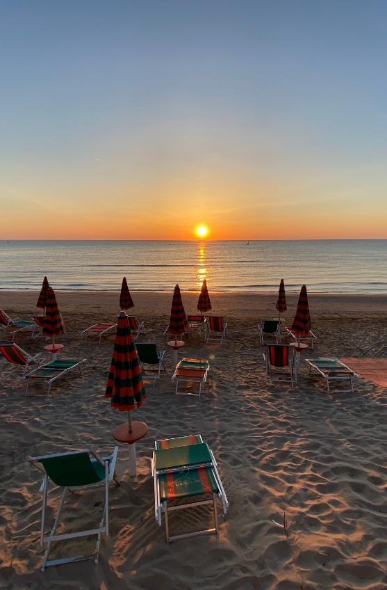 Alba serena su spiaggia deserta, ombrelloni chiusi, luce calda riflessa sul mare.