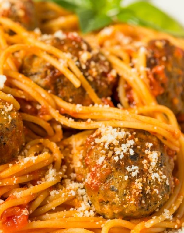Spaghetti al pomodoro con polpette, cosparsi di formaggio, evocano calore e tradizione italiana.