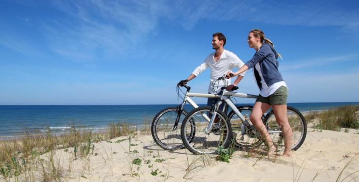 Coppia felice in bici sulla spiaggia, godendo il sole e la brezza marina.