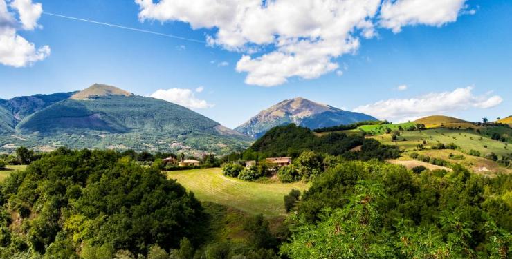 Colline verdi e montagne sotto un cielo azzurro evocano serenità e libertà.