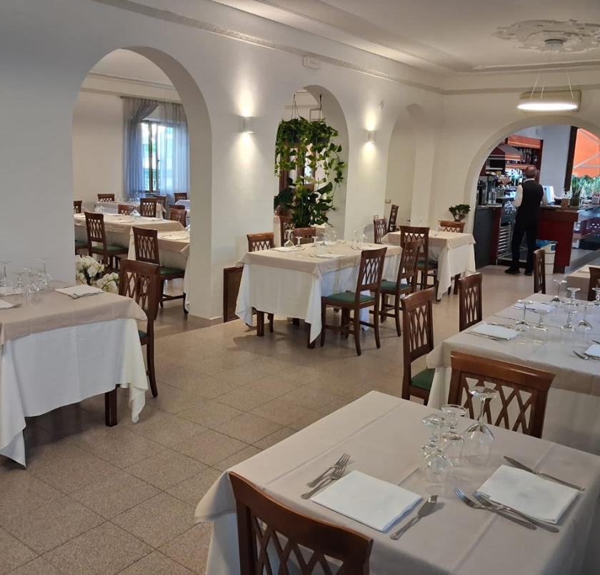 Ristorante elegante, tavoli apparecchiati, atmosfera accogliente, luci soffuse, piante decorative, barista al lavoro.