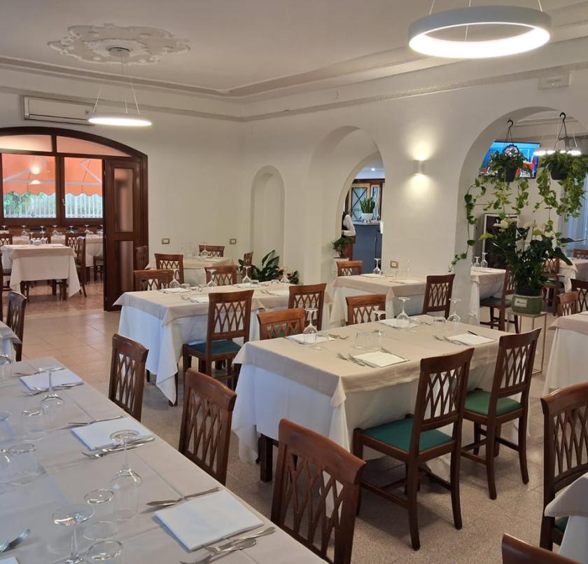 Ristorante elegante, tavoli apparecchiati, atmosfera accogliente con piante e luci soffuse.